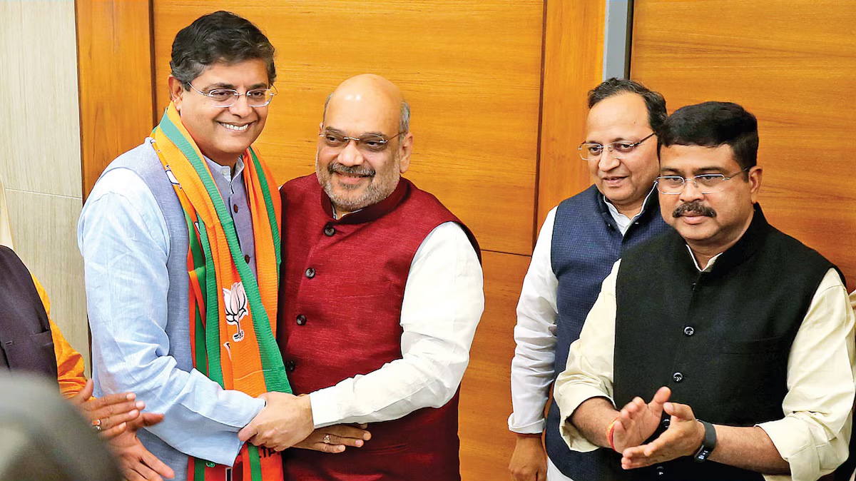 Baijayant Panda, wearing a BJP scarf, shakes hands with Amit Shah at the BJP headquarters as other party leaders applaud