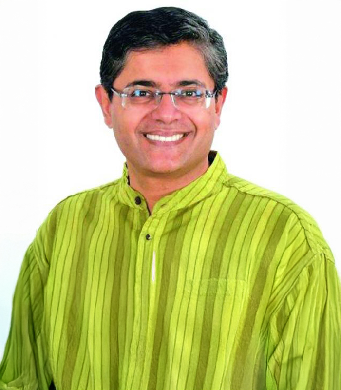 Portrait of Baijayant Panda smiling, wearing rimless glasses and a green striped kurta, photographed against a plain white background
