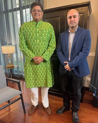 Baijayant Panda in a green printed kurta standing beside a man in a blue blazer in a wood-floored room