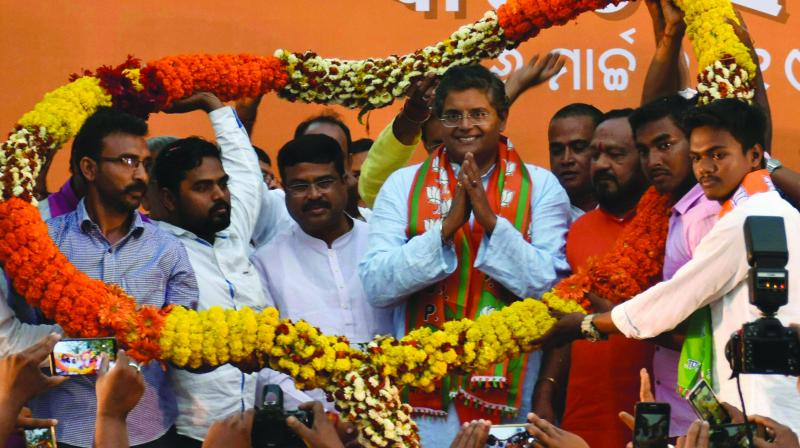Baijayant Panda with folded hands, wearing a saffron and green stole, as party workers raise long marigold garlands around him on a stage