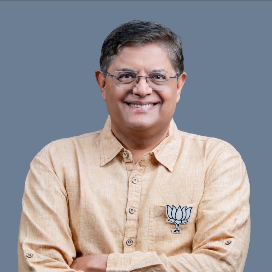 Official portrait of Baijayant Panda smiling with arms folded, wearing glasses and a light linen shirt with a BJP lotus badge, against a slate-grey background