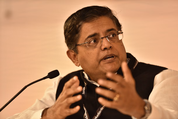 Baijayant Panda gesturing with both hands as he speaks at a panel, wearing glasses and a dark waistcoat with a lanyard, a microphone in front of him