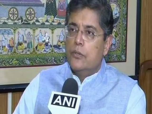Baijayant Panda in a light blue waistcoat speaking into an ANI microphone, in front of a Pattachitra painting