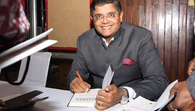 Baijayant Panda in a grey bandhgala smiling while signing a copy of his book at a table